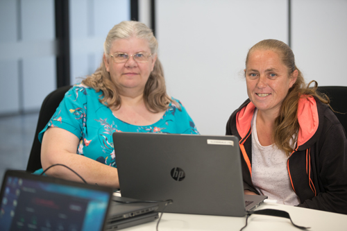 Two women sitting at a laptop smiling
