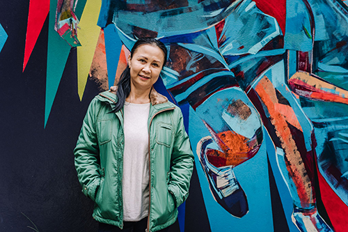 Woman in green jacket in front of graffiti wall.